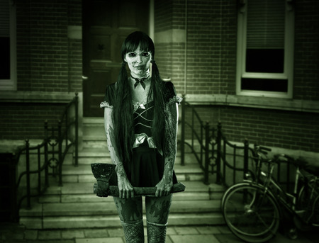 Halloween horror. Scary woman ghost with ax on porch of houseの写真素材