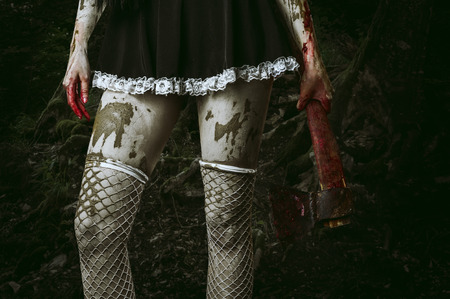 Halloween horror. Dirty woman's hand holding a bloody ax outdoor in forestの写真素材