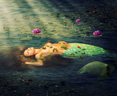 Beautiful woman mermaid with a fish tail resting in the water of the pond of liliesの写真素材