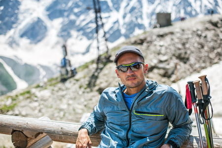 Young man mountaineer sitting on a snow hillside near top of mount Cheget. Mountain Donguzorun on...