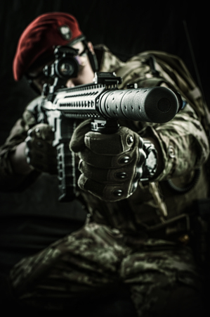 Young handsome military man in italian camouflage aiming from automatic rifle, he wearing red beret and gloves. Focus on the gun muzzleの写真素材