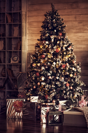 Christmas tree in dark room at home with lights, decorations and gift boxes - card.の写真素材