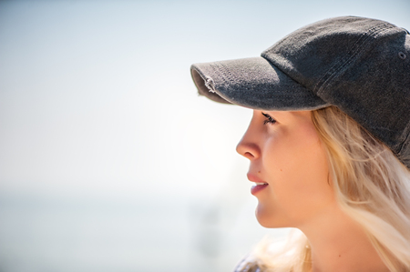 Defocus portrait of Beautiful girl close-up in profile in a cap against the seaの写真素材