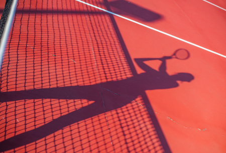 Tennis competition concept shadow of Woman holding racket playing tennis and waiting for the service while standing on court during matchの写真素材
