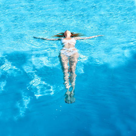 Beautiful young slim woman wearing fashion white swimsuit monokini swimming on back and relax in...