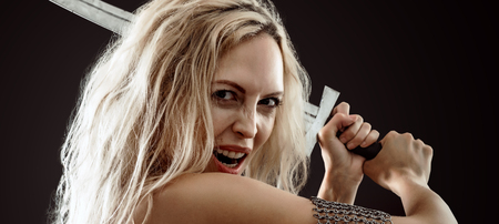 beautiful sexy warrior viking girl with a sword in hands attack and screaming on a black backgroundの写真素材