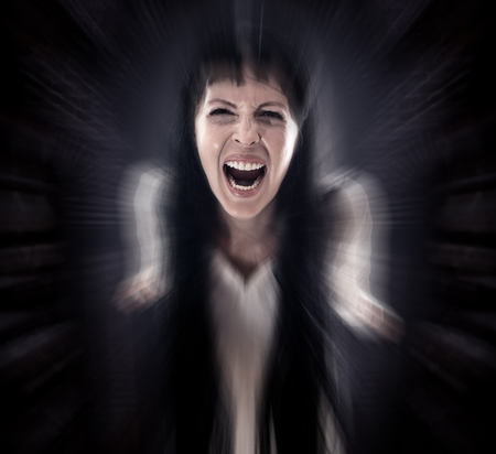 Halloween horror. Crazy bloody scary zombie woman looks into the camera and screams on black backgroundの写真素材