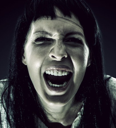 Halloween horror. Crazy bloody scary zombie woman looks into the camera and screams on black backgroundの写真素材