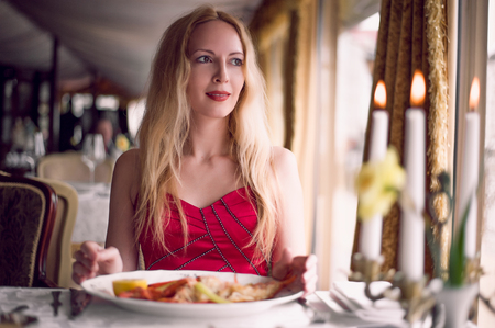 beautiful fashion woman in red dress sitting in expensive interior of cafe or restaurantの写真素材
