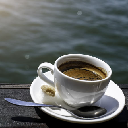A small white porcelain espresso cup on a saucer with a teaspoon and two pieces of white and cane sugarの写真素材
