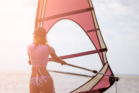 Beautiful girl windsurfer. Woman sportsman windsurfer on the sea surface at sunset timeの写真素材