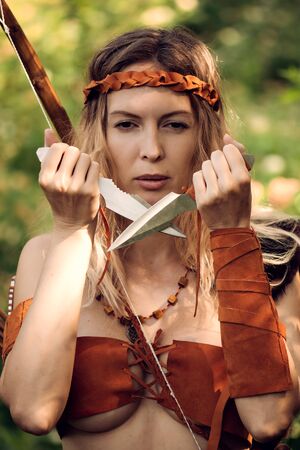 Beautiful girl archer with long blond hair with a bow and arrowson a back holding two steel knifes cold armsの写真素材