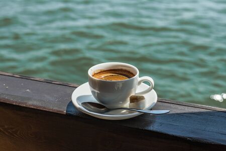 A small white porcelain espresso cup on a saucer with a teaspoon and two pieces of white and cane...