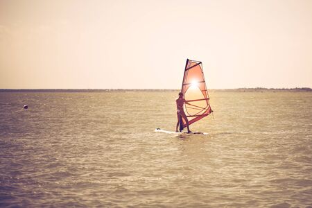 Young athletic slim girl sails on a windsurf board in the open sea on summer vacation at the resort. Windsurfingの写真素材