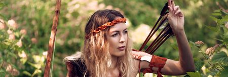 Beautiful girl archer with long blond hair with a bow and arrows dressed in leather and wristwear...