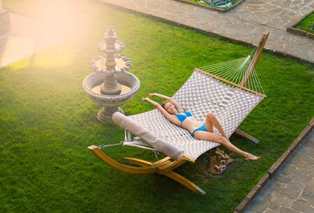 Slender beautiful young woman in a swimsuit is lying on a wicker hammock in the yardの写真素材