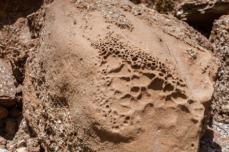 clay and sand on a stone with holes and dimples formed from wind and weather