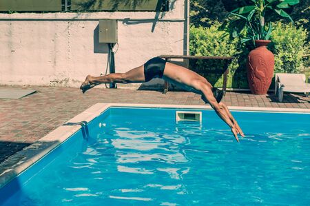 A young man with a slim athletic figure dives into the water with a pike from the side of the pool