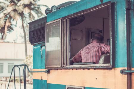 The driver sits in the train cabin. A blue old train stands on the tracks of a railway station in Galle Sri Lankaの写真素材