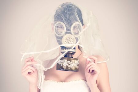 cyberpunk Bride in veil dress and protective mask in a gas mask with rhinestones style posing on a delicate backgroundの写真素材