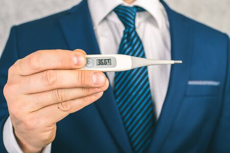 A man in a suit and tie holds in his hands an electronic thermometer with temperature 36.6. Man is healthyの写真素材