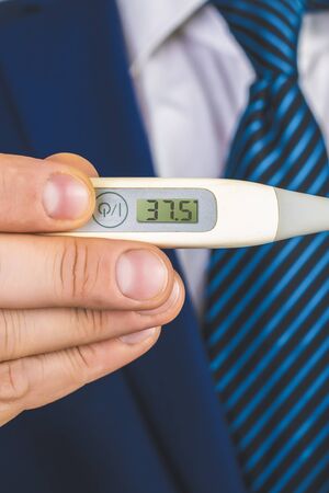 A man in a suit and tie holds in his hands an electronic thermometer with temperature 37.5 Human is...