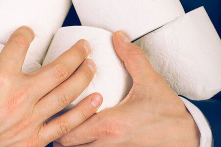 A man in a blue business suit holds 5 rolls of white toilet paper in his hands