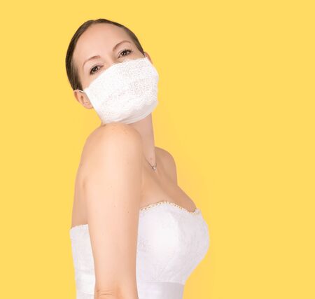 Beautiful young bride in a wedding dress and a white medical mask on her faceの写真素材