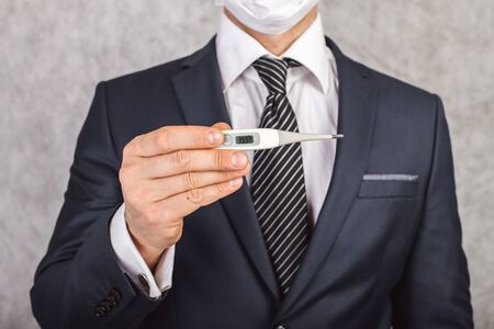 A man in a suit and tie holds in his hands an electronic thermometer with temperature 39.5の写真素材