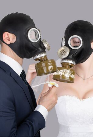 Bride and groom in protective gas masks posing on a grayの写真素材