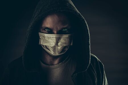 Dark photo of Young handsome man wearing medical protective face mask and hood in the nightの写真素材
