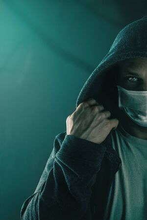 Young handsome man wearing medical protective face mask and hood in the night