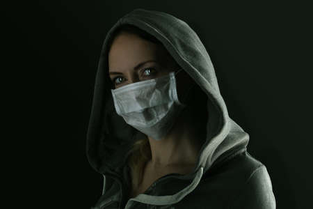 Young serious woman wearing medical protective face mask and hood in the nightの写真素材