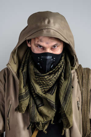 Young handsome man wearing black protective face mask and jacket with hood on gray