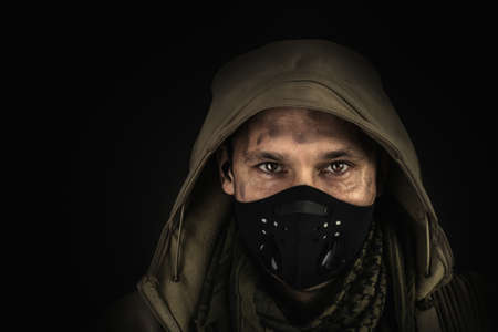 Dark photo of Young handsome man wearing black protactive face mask and hood on black background
