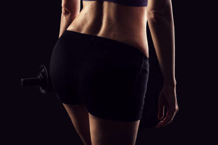 Slim athletic woman Holding dumbbell in the hand on blackの写真素材