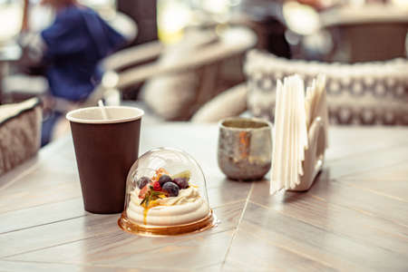 Fruit cake with cream and meringue in plastic round box and eco-friendly paper cup of coffee or tea in a street cafeの写真素材
