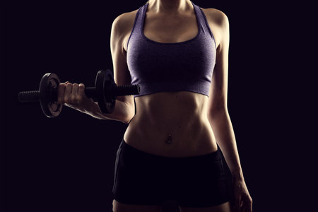 Slim athletic woman Holding dumbbell in the hand on blackの写真素材