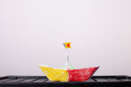 Children's boat made of paper, yellow and red, on a white background, indoors, on a black table