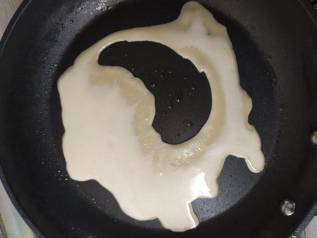 Unbaked pancake batter of a funny shape in a black pan