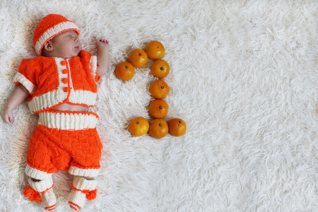 One month baby. Sleeping  newborn baby one month old  in orange knitted costume on white fur blanket with numeral one next to him and space for text. Greeting card or invitation..の写真素材