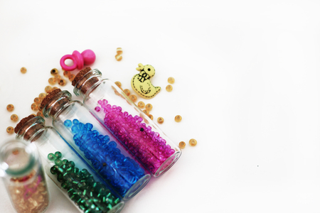 Tiny glass bottles filled with colorful beads and elements for a baby spilling out, isolated on...