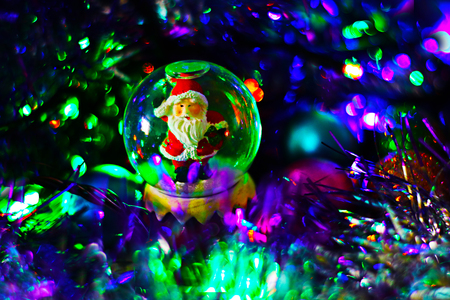 Glass snowball with santa claus inside on festive blurred background with sparkling lights and tinsel. Christmas and new year magical background, template.の写真素材