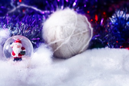 Christmas and new year background with santa claus in glass ball, white yarn on soft defocused snowy background with tinsel.の写真素材