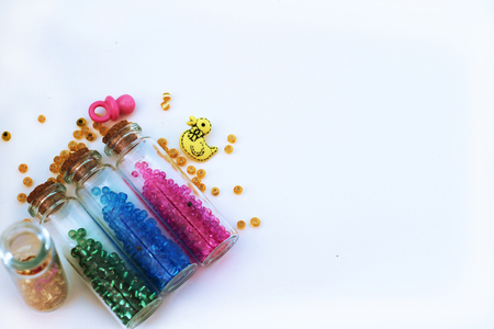 Tiny glass bottles filled with  colored  beads and elements for baby  spilling out, isolated on a white background with space for text. の写真素材