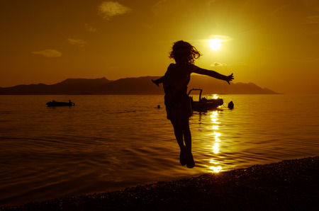 silhouette of jumping girl on beach at sunsetの写真素材