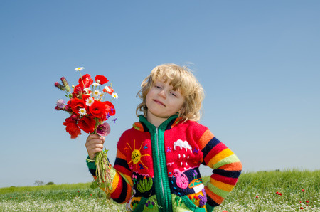 blond beautiful child on white daisy meadow  with bunch of flowersの写真素材