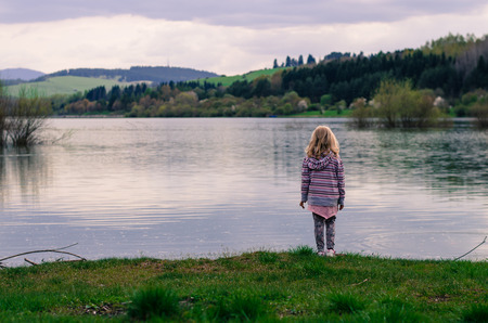 blond girl standing in the waterside of pond in the afternoonの写真素材