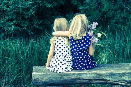 two  blond girls sitting on bench back viewの写真素材