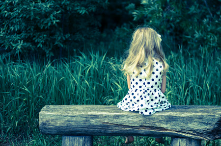 girl with long blond hair sitting in bench and waiting filtered effect back viewの写真素材
